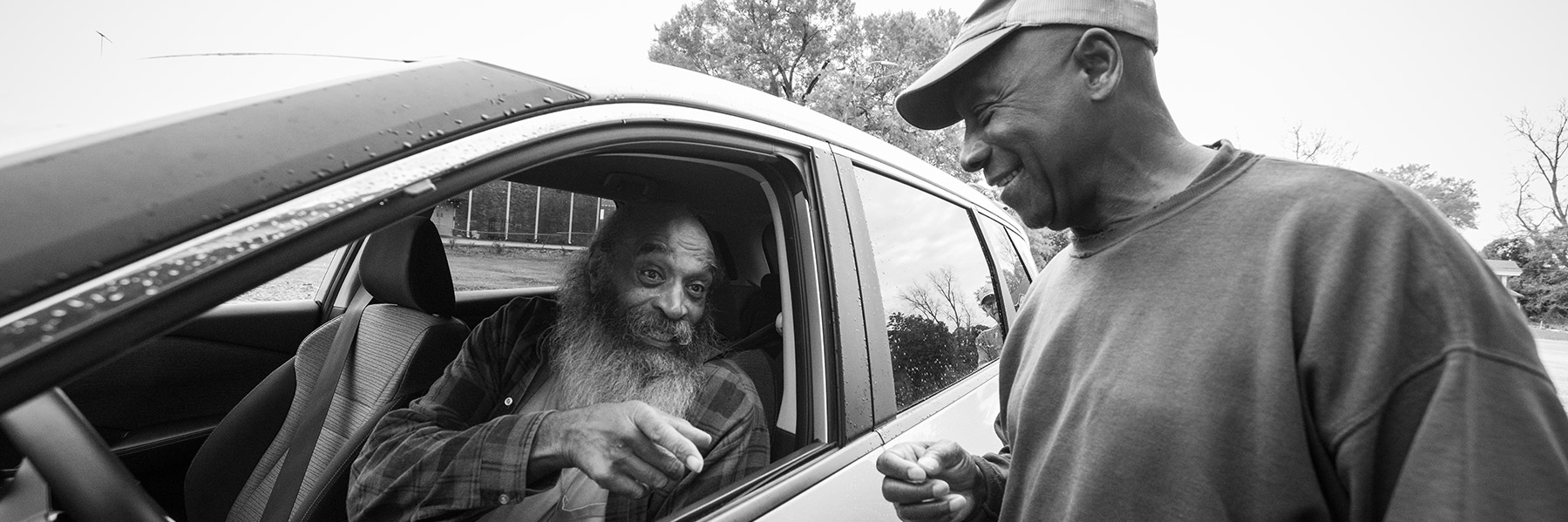 two men talking, one is inside a car.